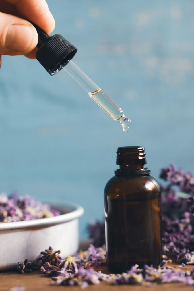 Bottle with aroma oil and lavender flowers on blue background